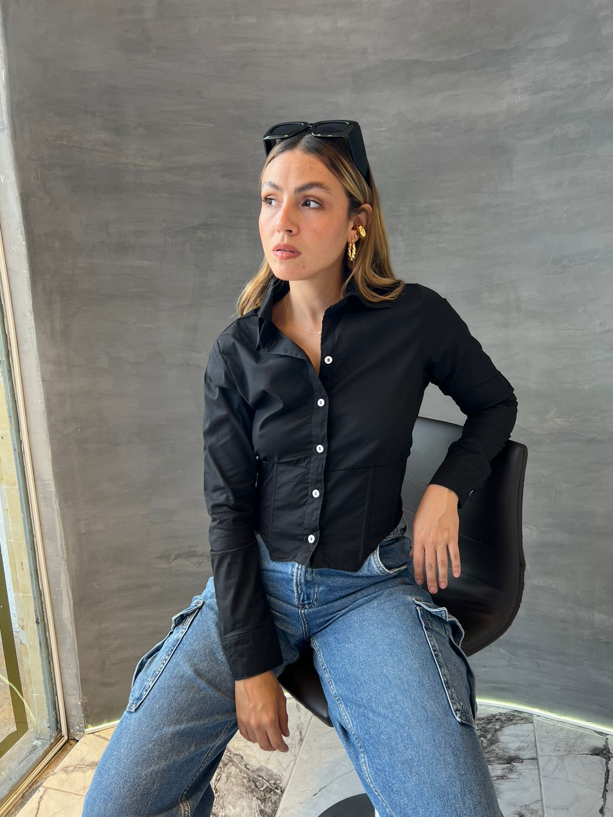 Mujer vistiendo una blusa crop top negra con botones blancos, ideal para un look elegante y moderno. Disponible en KIKE RODRIGUEZ.
