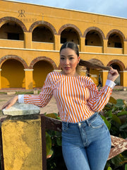 Mujer con blusa naranja con espalda descubierta disfrutando de una vista panorámica. Blusa ideal para un look casual y chic. Disponible en KIKE RODRIGUEZ.