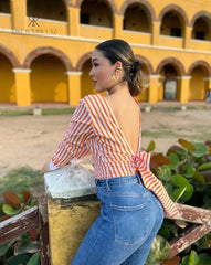 Mujer con blusa naranja con espalda descubierta disfrutando de una vista panorámica. Blusa ideal para un look casual y chic. Disponible en KIKE RODRIGUEZ.