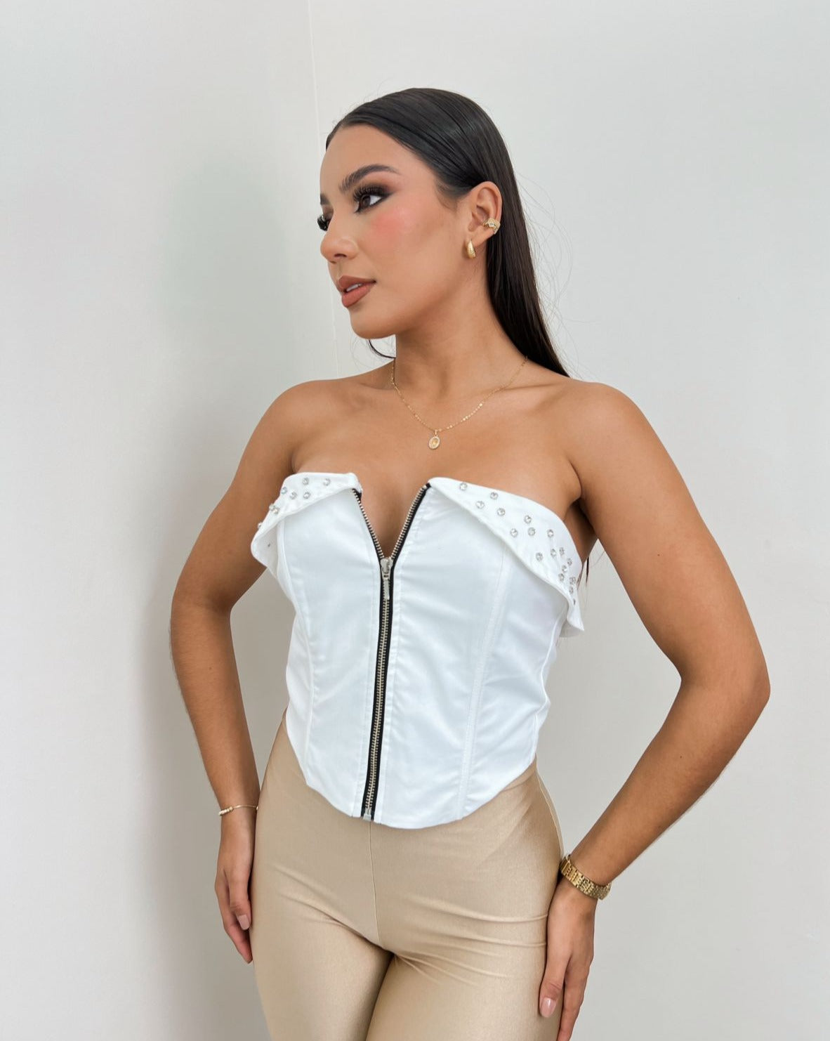 Mujer vistiendo un corset blanco con cierre frontal y detalle de tachuelas, ideal para un look atrevido y moderno. Disponible en KIKE RODRIGUEZ.