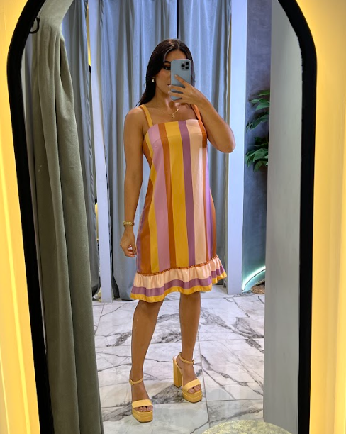 Mujer posando frente al espejo con un vestido a rayas multicolor y volantes en el dobladillo, ideal para el verano y ocasiones casuales.