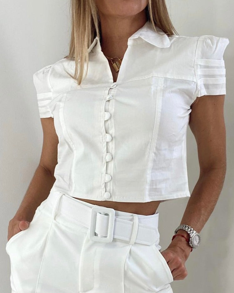 Mujer con blusa blanca de manga corta y botones decorativos, ideal para un look elegante y moderno. Disponibilidad en KIKE RODRIGUEZ.